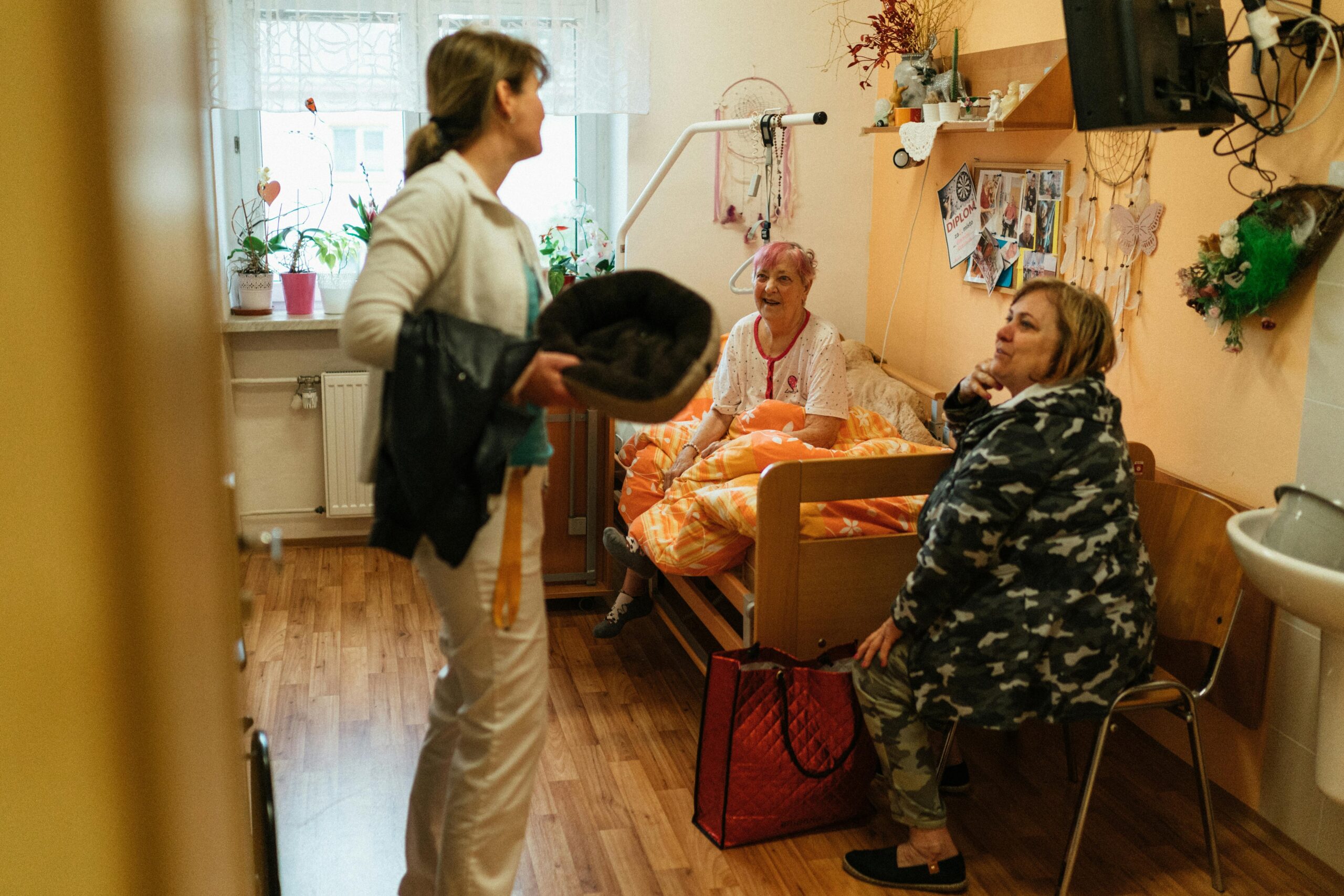 Three women conversing in a cozy elderly care room, fostering warmth and togetherness.