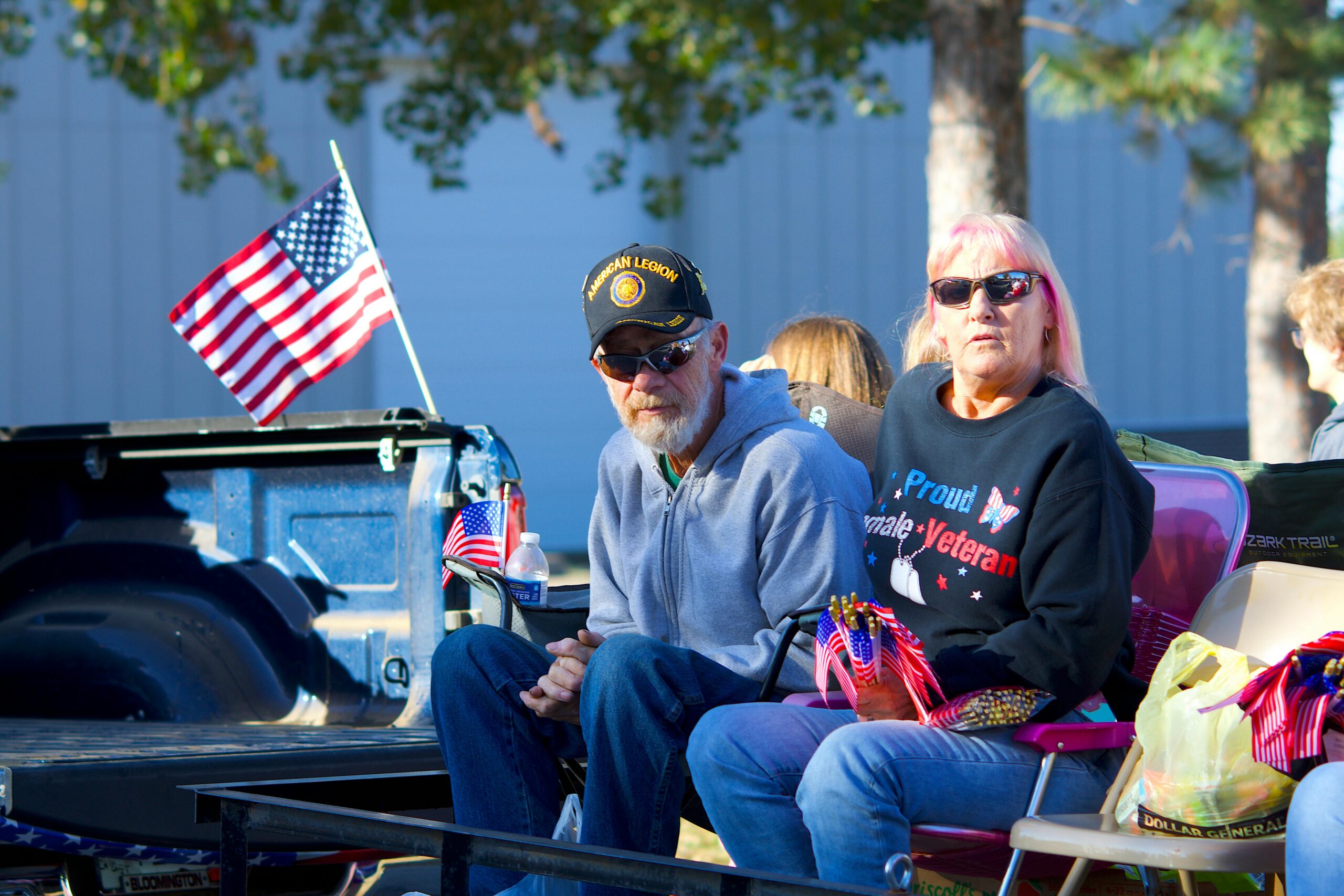 Senior veteran couple in a parade setting with American flags, showcasing patriotism and community spirit.